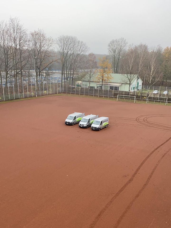 Firmenfahrzeuge auf Sportplatz vor Flutlichtinstallation