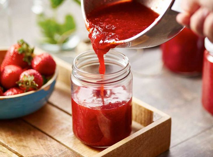 Handwerkliche Herstellung: Erdbeermarmelade wird in ein Glas gegossen