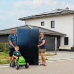 Familie mit Solarmodul vor ihrem Haus