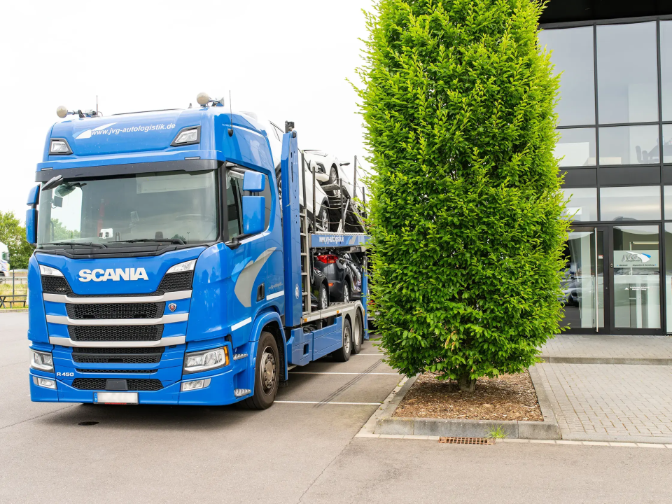 Blauer Scania Lkw mit Auflieger vor dem Firmengebäude