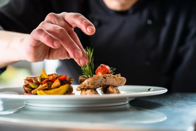 Koch garniert ein Gericht mit Schweinefleisch und Gemüse