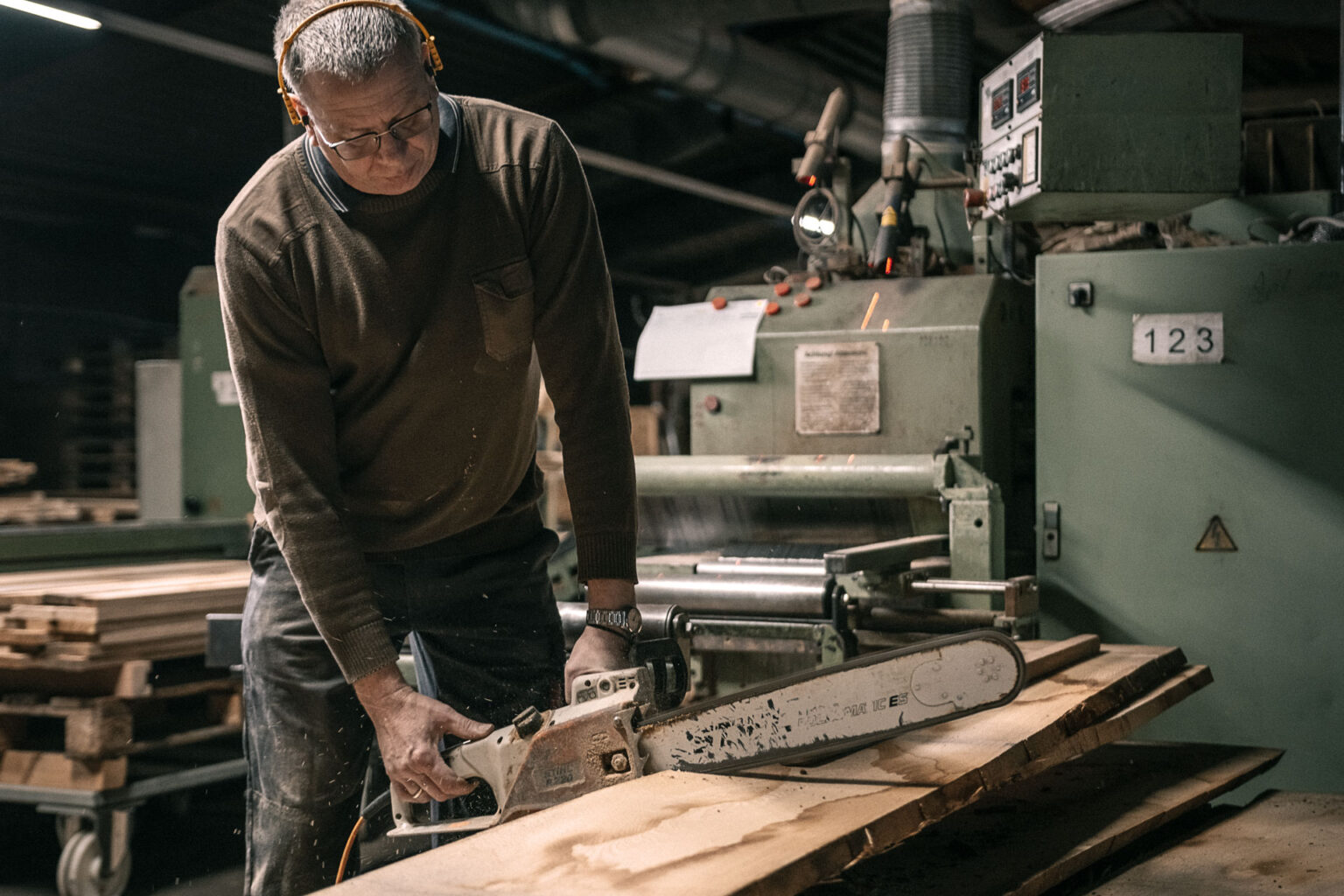 Carpenter splitting a wooden board in the middle with the chainsaw