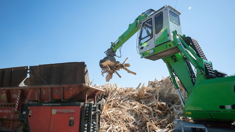 Holzstücke werden per Baggerarm in die Schleifmaschine eingebracht