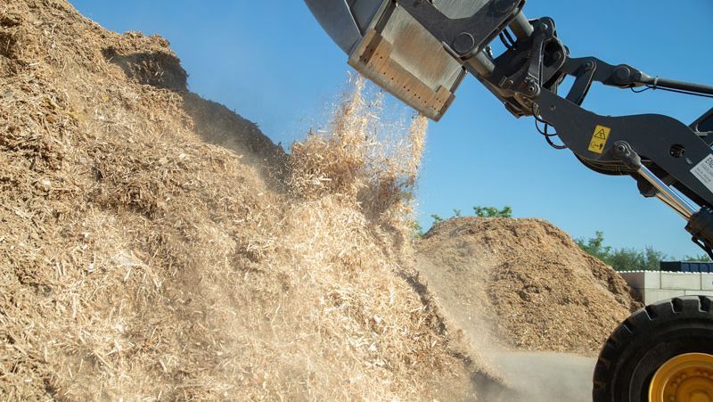 Frontlader kippt Holzhackschnitzel auf einen Materialhaufen