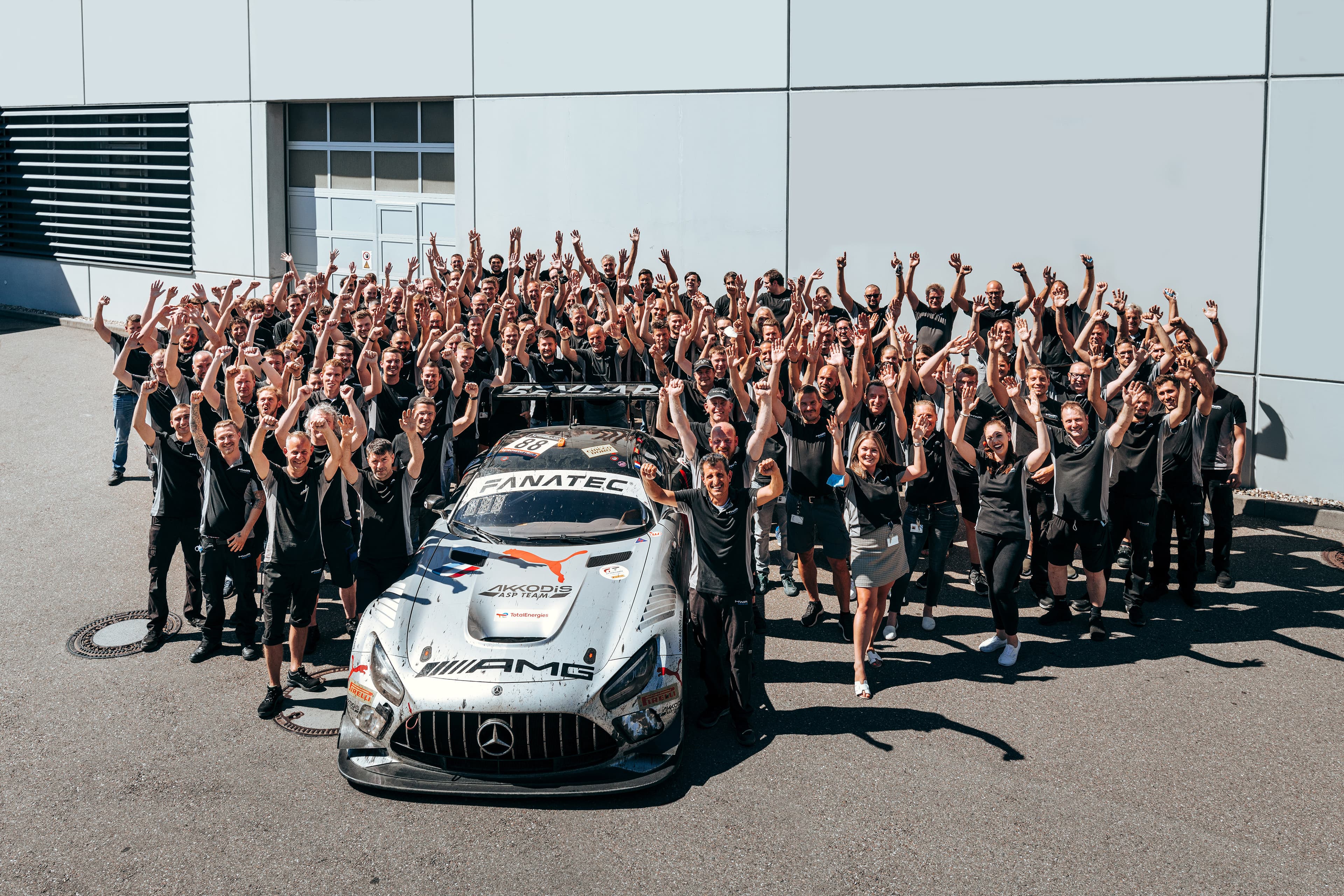 HWA Mitarbeitende mit Mercedes-AMG GT3 am Firmengebäude