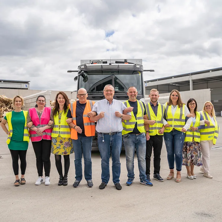 Team in Warnwesten vor einem Entsorgungsfahrzeug auf dem Betriebshof